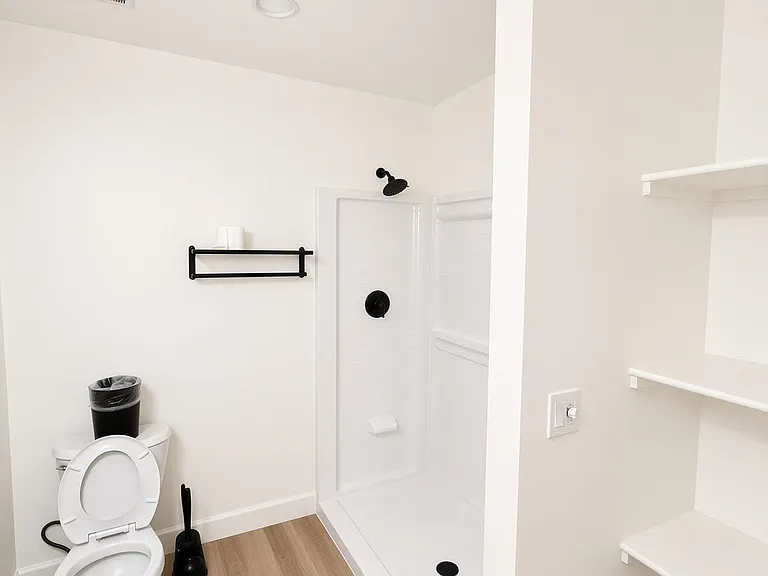 Clean full bath with walk-in shower, sleek fixtures, and built-in open shelving for linens and essentials.