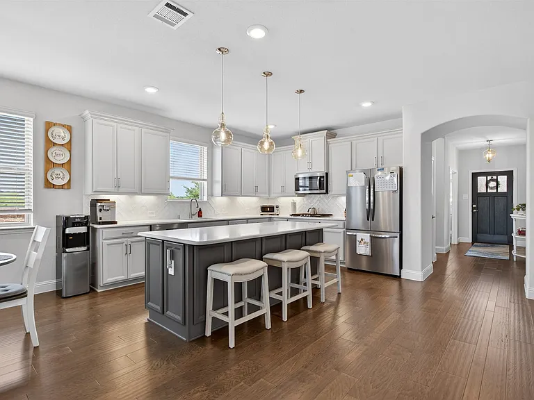 Kitchen featuring wood-finish flooring, an island with countertop seating, white cabinetry, a tile backsplash, and stainless steel appliances