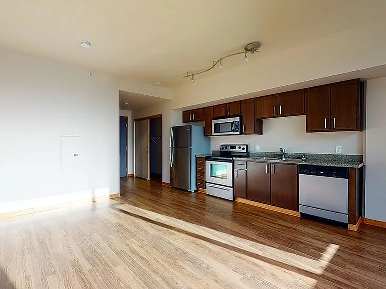 Apartment Kitchen with Stainless Steel Appliances, Dining and Living Room with Wood-Style Flooring.