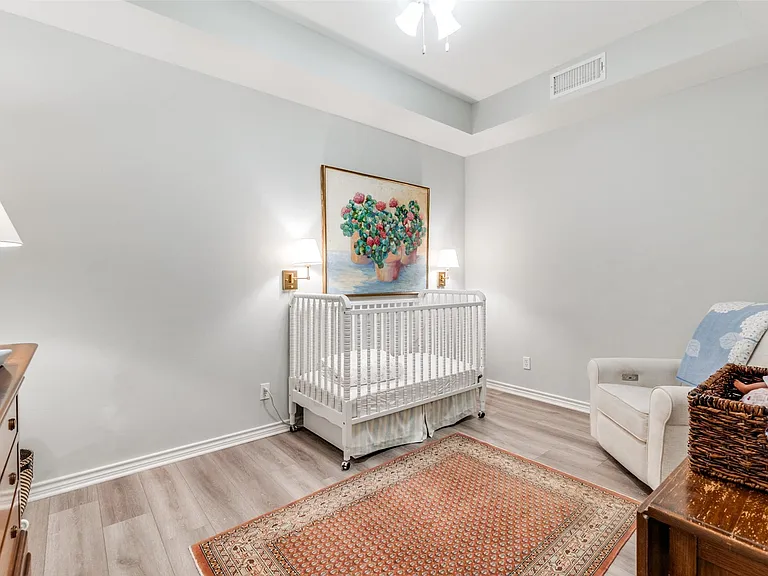 Spacious room featuring light gray walls, white baseboards, wood-finish flooring, and a tray ceiling with a ceiling fan