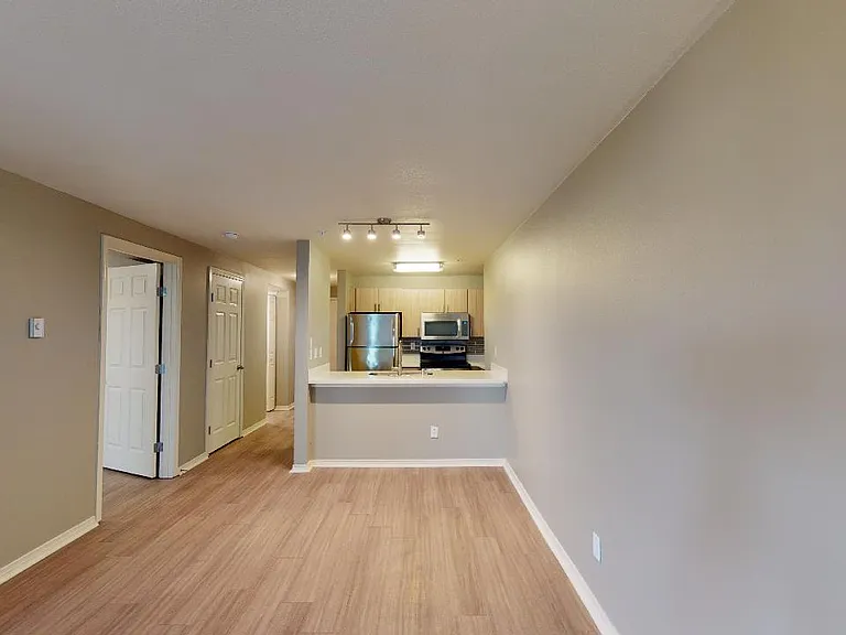 Apartment kitchen with stainless steel appliances, dining and living room with wood-style flooring.