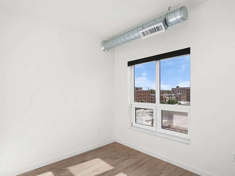 Bright, minimalist room with large window offering stunning urban views and sleek wooden flooring. Bright, minimalist room with large window offering stunning urban views and sleek wooden flooring.