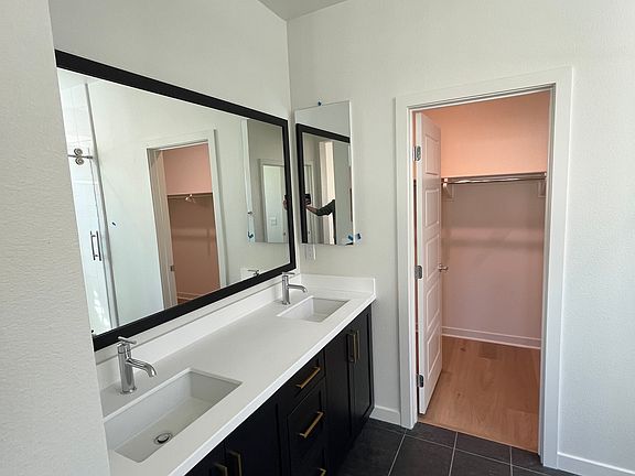 Primary bathroom with double sinks, walk-in closet, sliding shower doors, and private toilet area.