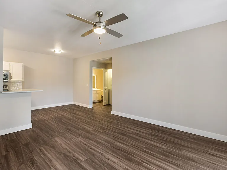 Experience cozy comfort in our living room, complete with a gentle ceiling fan overhead and a glimpse of our stylish kitchen in the background