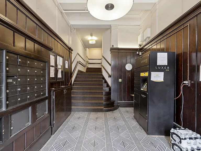 Entrance hall featuring wooden paneling, mailboxes, staircase, and a Luxer package locker against a patterned floor
