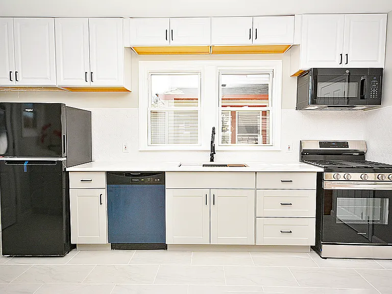 Brand new kitchen with quartz counters, modern appliances, and large workstation sink with cutting board, roll up drying rack, and stainless steel colander.