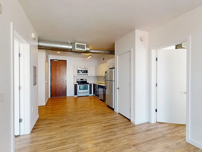 Apartment kitchen with stainless steel appliances, dining and living room with wood-style flooring.