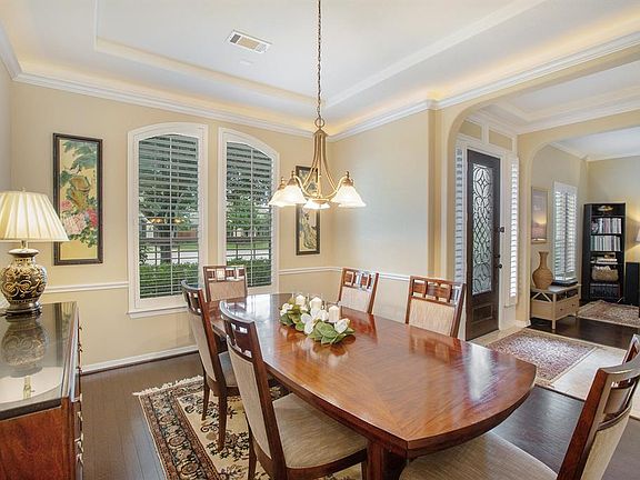 Formal dining room just off the entry features a tray ceiling, crown molding with lighting, plantation shutters, chair rail and hardwood flooring.