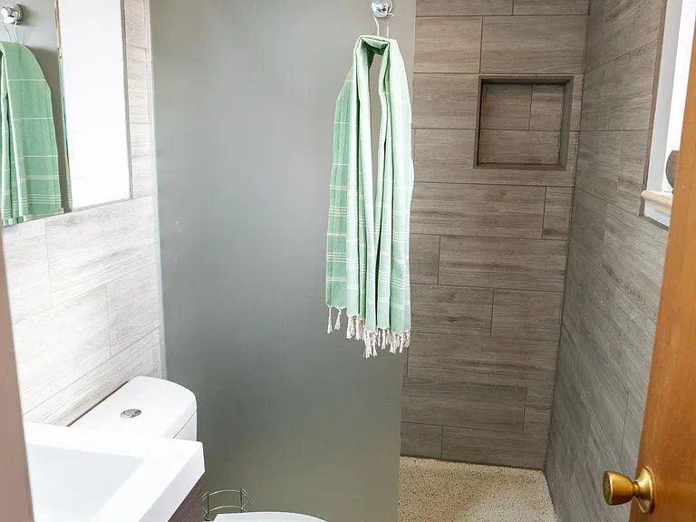 Primary bathroom with thermostatic shower, vanity, sink, toilet, and medicine cabinet. There is a west-facing window on the right.