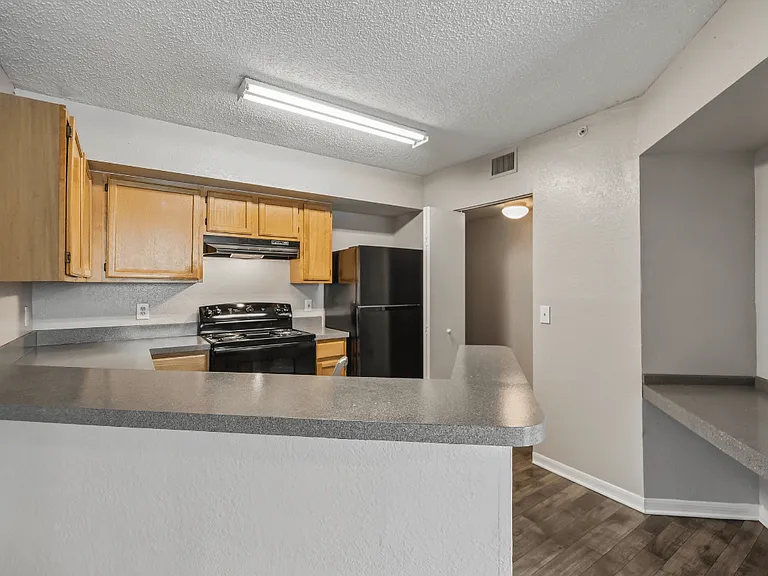 Kitchen with natural wood cabinetry, black appliances, generous counter space, and breakfast bar in a 1-bedroom apartment at Gregory Cove in Jacksonville, FL.