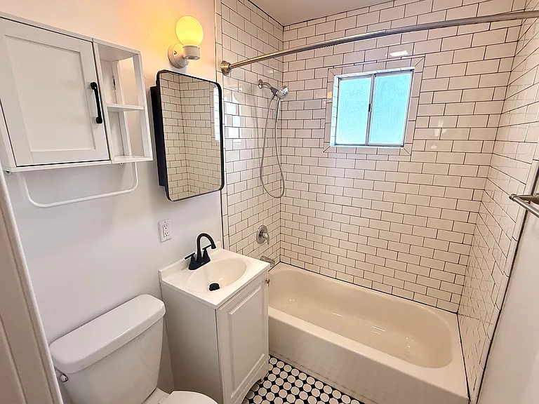 Bathroom with spray wand, black faucet and vanity mirror, vintage style floor tile and subaway tile shower surround.
