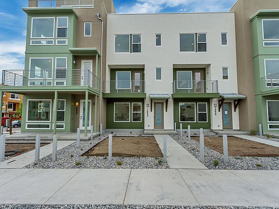 Modern three-story townhouses with green accents, large windows, and balconies. The landscaping is u