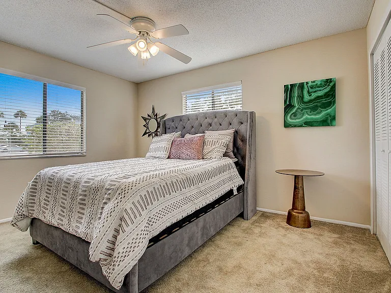 Bright and cozy bedroom with elegant decor, featuring a plush bed, stylish artwork, and ample natural light from large windows.