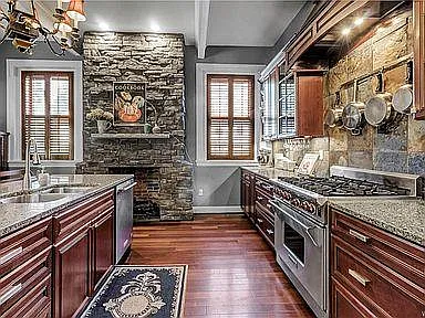 kitchen with granite countertops, island with sink and dishwasher, Wolf 6 burner stove, and stone gas fireplace