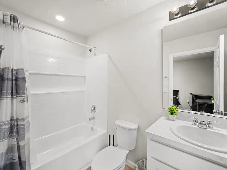 Full bath with tub/shower combo, built-in wall shelving, and a single-sink vanity with mirrored storage.