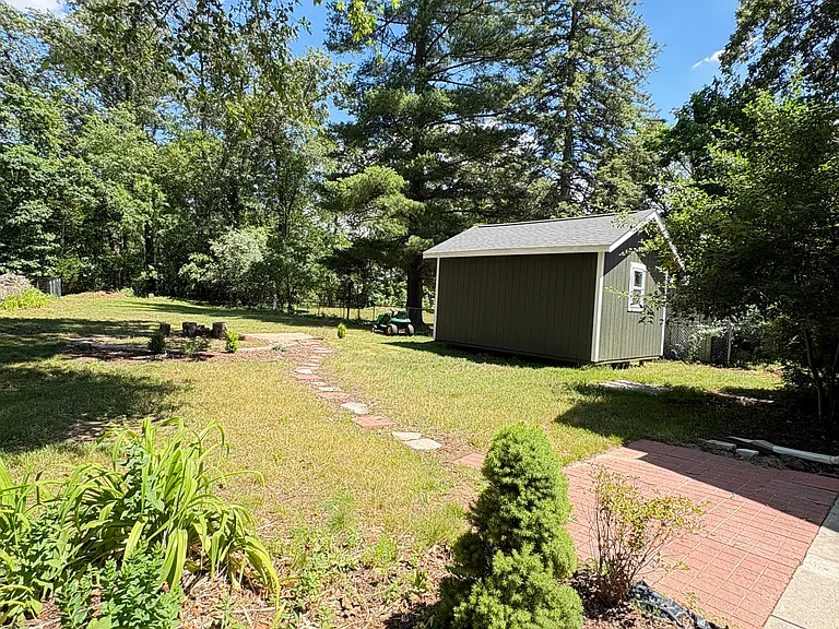 The spacious backyard features landscaped beds and a fire pit area, creating a welcoming space to enjoy the outdoors. Please note: the green and white shed is reserved for landlord management equipment storage and is not included with the rental property.