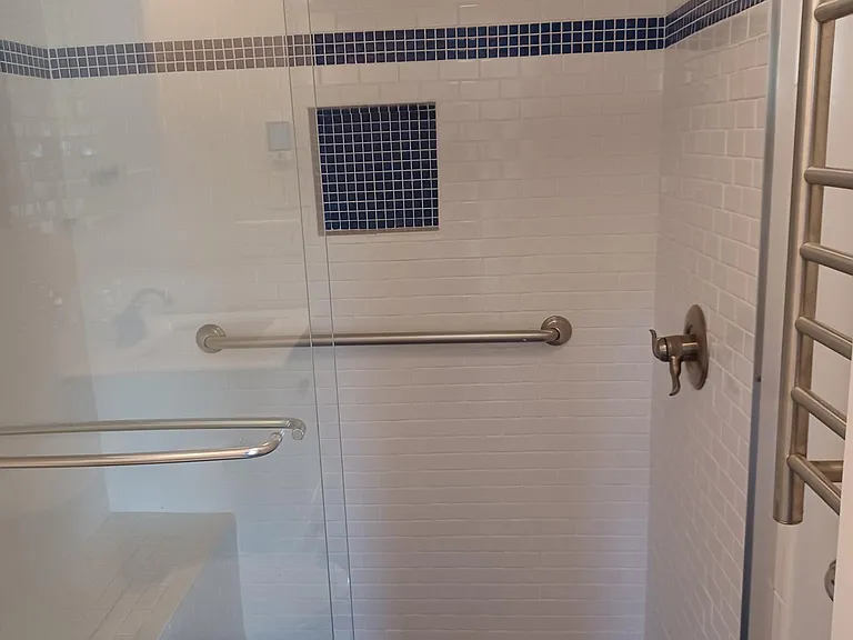 large shower with built in tile bench and hand rails for safety