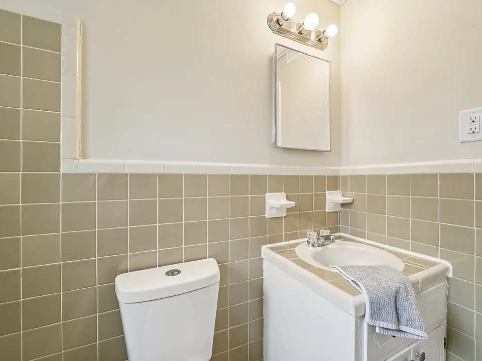 Full size tube, shower, with the charm of original tile, sink, toilet, and medicine cabinet with shelves.