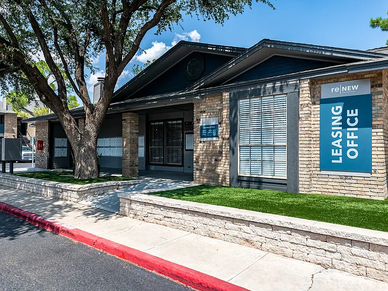 The front of a leasing office is shown partially shaded by a large, mature tree.