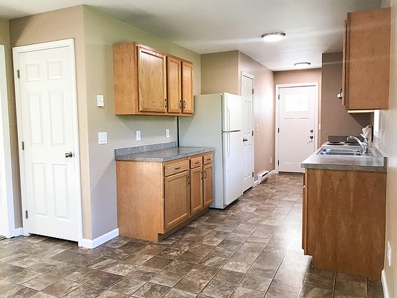 The kitchen has doors leading to the driveway and the basement. A pantry closet is next to the refrigerator. Across from the pantry is a bench, shelf, and coat hooks.