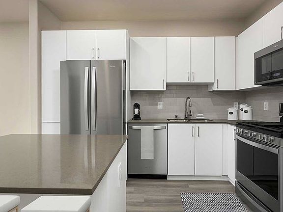 Renovated Package I kitchen with quartz countertops, white cabinetry, stainless steel appliances, hard surface vinyl plank flooring, and tile backsplash