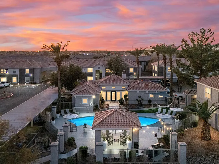 An enchanting aerial view of Sedona Peaks as the sun sets, casting a vibrant glow over the sky. The shimmering resort-style pool, elegant cabana seating, and palm-lined pathways create a serene escape, perfect for unwinding after a long day.