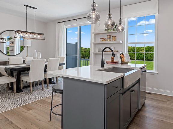 Gray kitchen island with apron sink, white counters, light wood floors, spacious dining area with sl