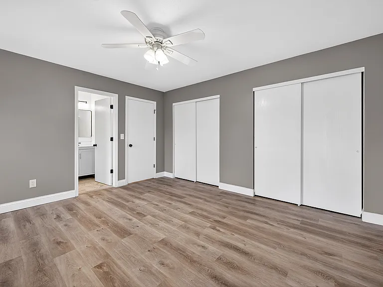 Unfurnished bedroom featuring multiple closets, wood flooring, ceiling fan, and en-suite bath