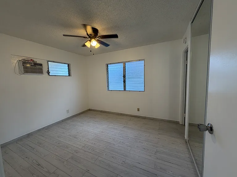 Primary bedroom, small window ac unit and ceiling fan for cooling. Floor to ceiling mirrored closet doors keep room bright, en suite bath.