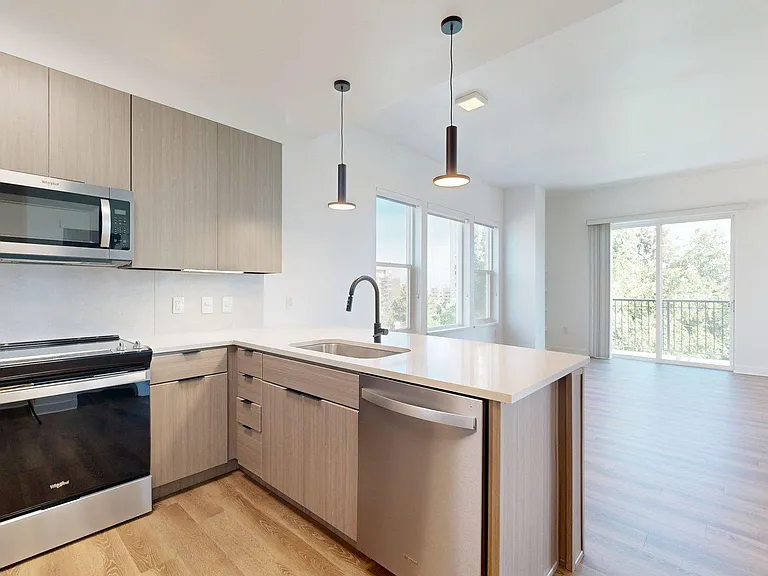 Apartment kitchen with stainless steel appliances, light counters, and wood style floor.