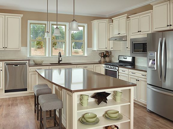 Island kitchen with cream cabinets, subway tile backsplash, stainless appliances and quartz countert