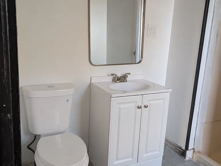 Bathroom view of the new toilet and vanity. The mirror is an AI generated placeholder and not the actual mirror. New mirror will be installed by move-in date.
