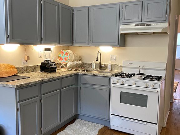 Kitchen has a large sink with pull-out sprayer, granite countertops and white refrigerator and stove. Stove has hood for added ventilation when cooking.