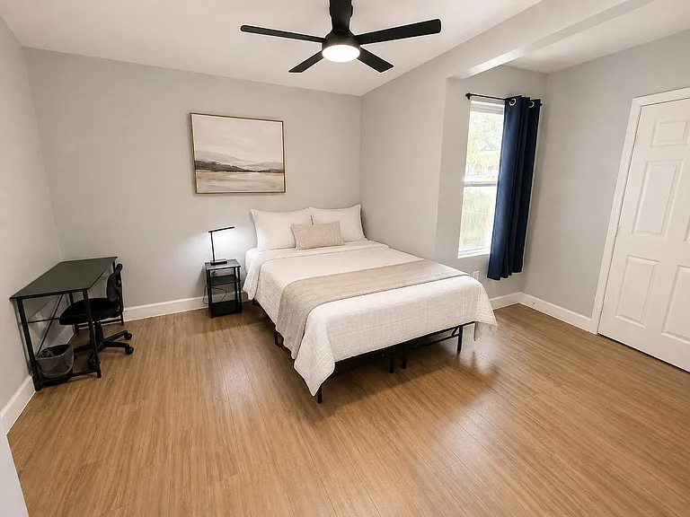 Furnished bedroom with full-size bed, dedicated desk area, ceiling fan, and window with curtains plus a roomy closet.