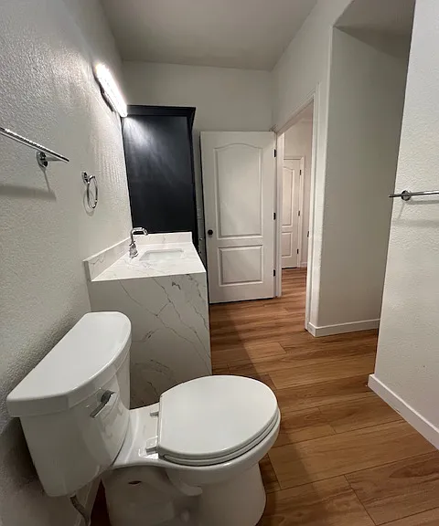View from inside the shower annd bathtub of new toilet, waterfall edge of the counter and new navy blue cabinetry . The cut out are to the right has hookuops for washer and dryer.