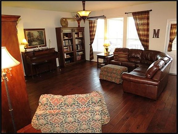 Family room with handscraped wood floors, ceiling fan and wall of windows. Drapery panels can stay.