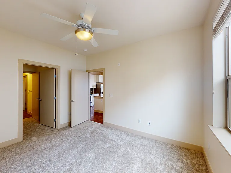 Spacious apartment bedroom with large closet, attached bathroom and plush carpet flooring.