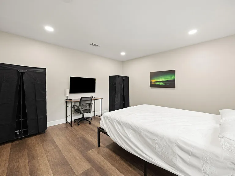 Private bedroom with wood-look flooring, a bed, and a dedicated desk setup, plus wardrobe storage for easy organization.