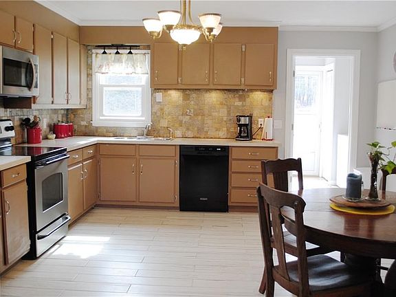 Large eat in kitchen with wood look ceramic tile floor, stone backsplash stainless appliances. Laundry room just off the kitchen leading outside.