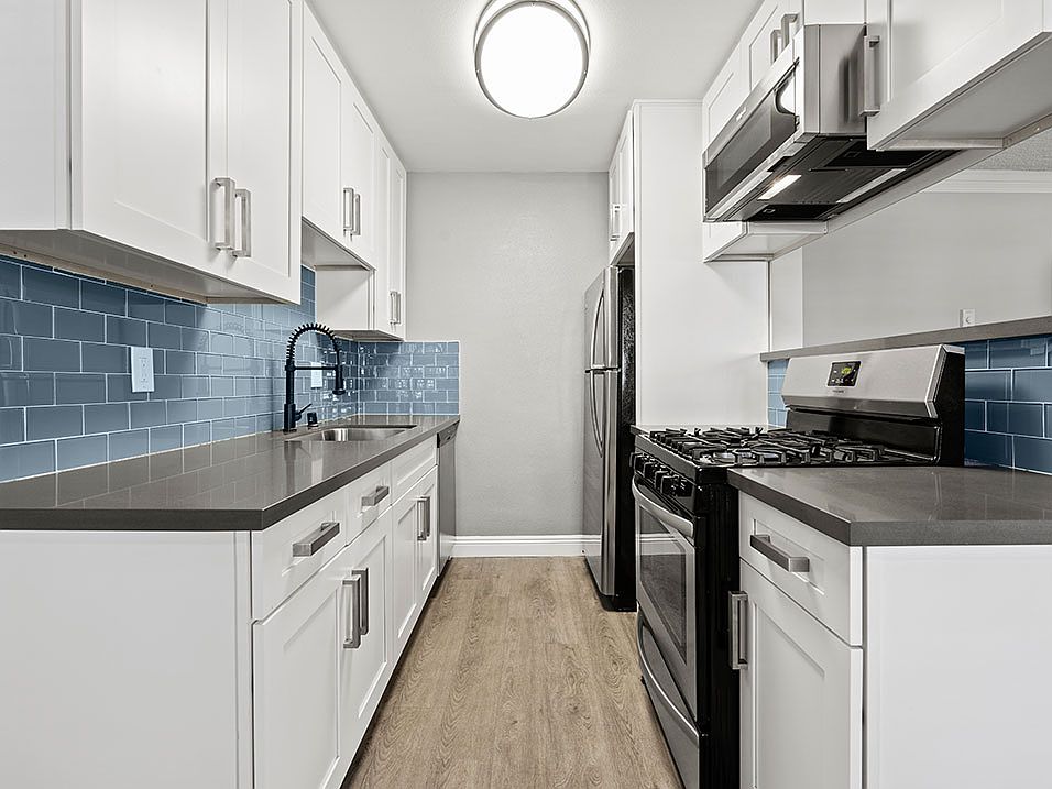 Blue tiled kitchen with stainless steel oven, microwave, and fridge.
