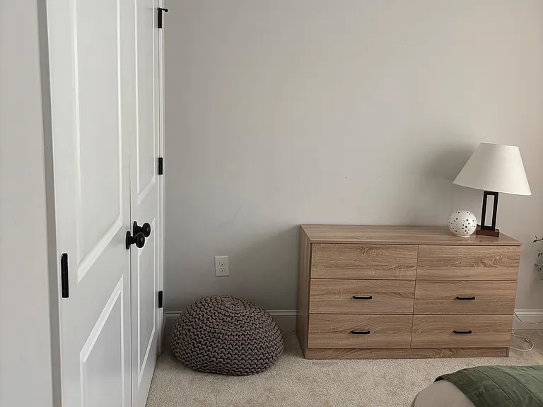 Carpeted bedroom area with a double-door closet and a dresser, offering practical storage and space for everyday essentials.