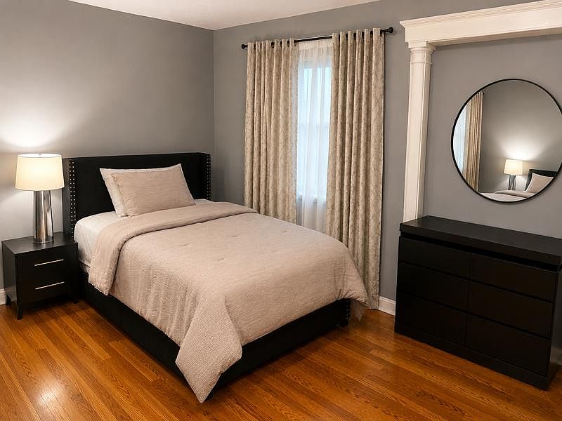 Well-appointed bedroom with hardwood floors, a full bed setup, blackout-style drapes, and a dresser with mirror.