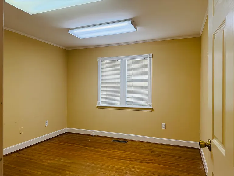 Bright, flexible room with warm neutral walls, natural light from the window and polished hardwood floors.