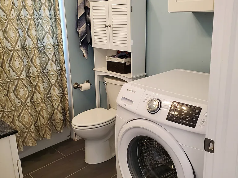 Washing machine in bathroom with storage cabinet overhead for storage
