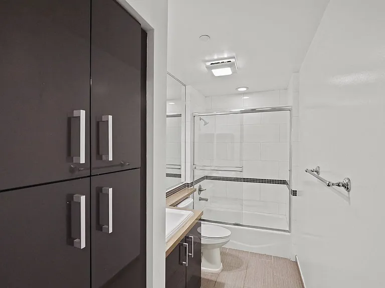 Bathroom with Full-Size Bathtub with Glass Door and Cabinet Storage