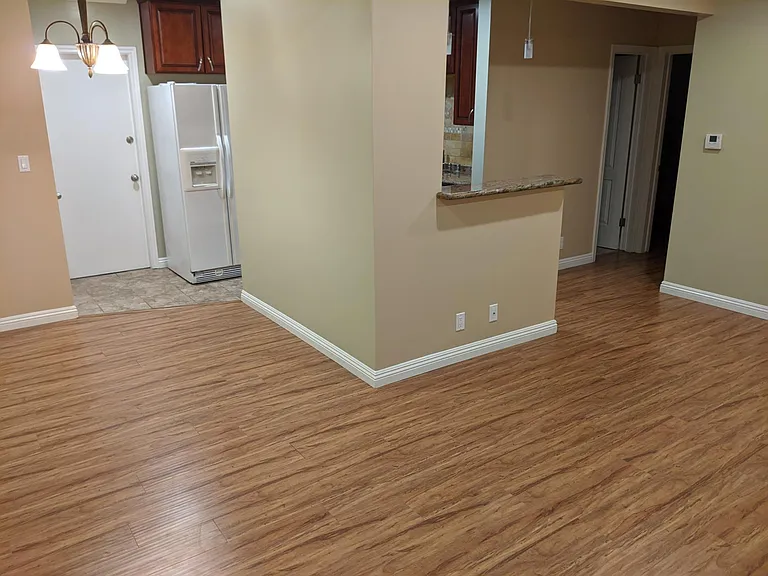 Main living room with view of kitchen and side door entrance. Hallway on the right heads to the bathroom and two bedrooms.