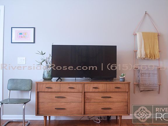Smart TV sitting on a vintage mid-century dresser. Extra blankets hanging on a wall ladder to snuggle up with and stream your favorite show.