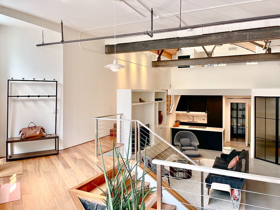 Open-concept living area with soaring vaulted ceiling, natural light from expansive skylights, and exposed brick walls.
