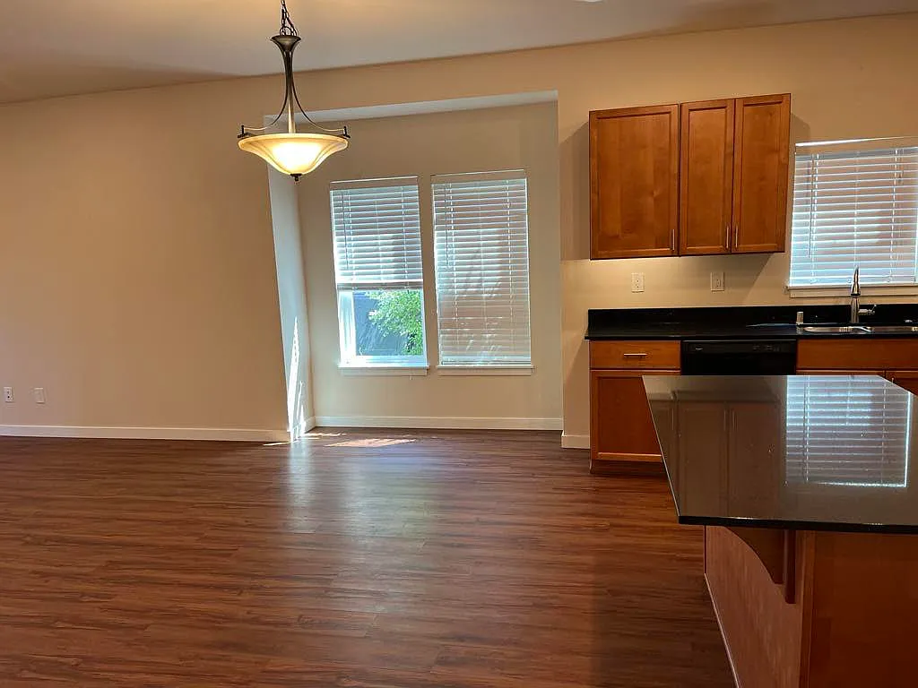 Bright open-concept kitchen and living area featuring durable LVP flooring, center island, ample cabinet space, cozy fireplace, and sliding glass doors that fill the space with natural light. - 700 Pine Ave #201