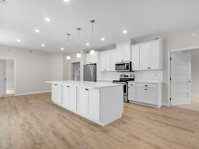 Modern kitchen with sleek white cabinetry, spacious island, and stainless steel appliances, enhanced by elegant pendant lighting. Modern kitchen with sleek white cabinetry, spacious island, and stainless steel appliances, enhanced by elegant pendant light